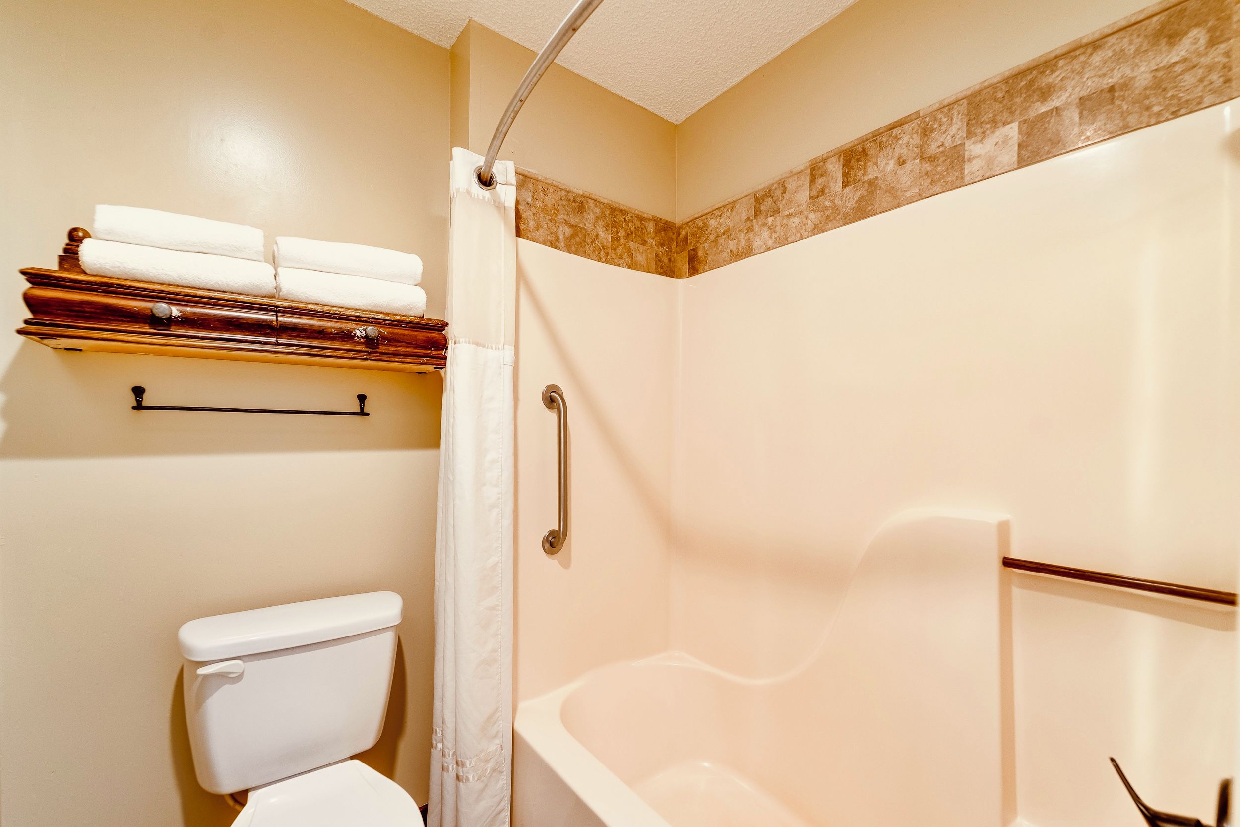 A bathroom with a toilet, a shower with a grab bar, and a towel rack with folded towels.