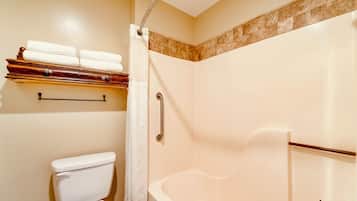 A bathroom with a toilet, a shower with a grab bar, and a towel rack with folded towels.