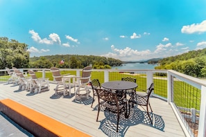 Une terrasse dotée de mobilier d’extérieur, d’une table ronde et de chaises, offrant une vue sur un lac et la verdure environnante.
