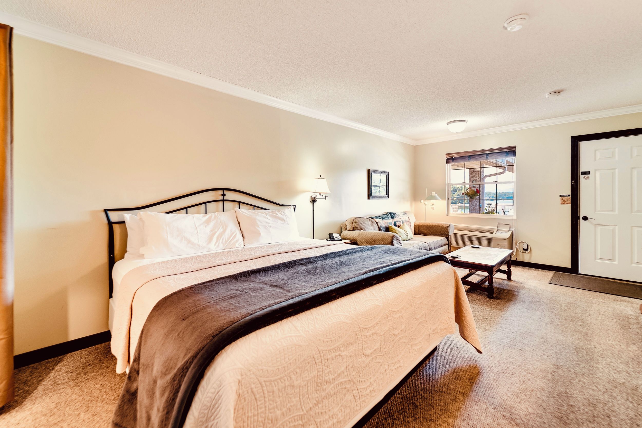 A bedroom with a bed, bedside table, lamp, window, and door.
