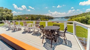 A deck with outdoor furniture, a round table, and chairs, overlooking a lake and greenery. - Deerfield Inn - King Bed w/ Sofa (Hayesville)