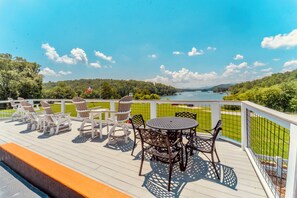 Une terrasse dotée de mobilier d’extérieur, d’une table ronde et de chaises, offrant une vue sur un lac et la verdure environnante.