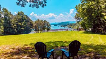 A grassy area with two chairs facing a scenic view of a lake and buildings in the distance.
