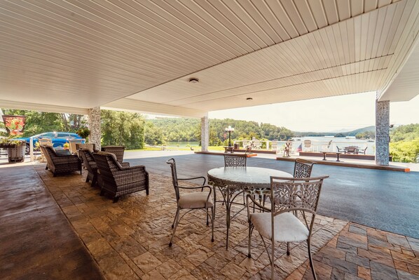 An outdoor patio with wicker furniture, a round table, and a view of a lake and mountains.