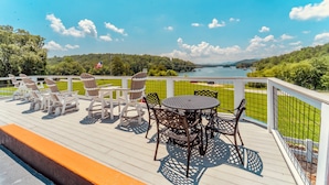A deck with outdoor furniture, a round table, and chairs, overlooking a lake and greenery. - Deerfield Inn - Two Queen Beds (Hayesville)
