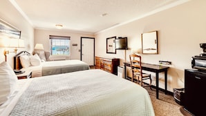 A hotel room with two beds, a desk, a television, and a window with a view. - Deerfield Inn - Two Queen Beds (Hayesville)