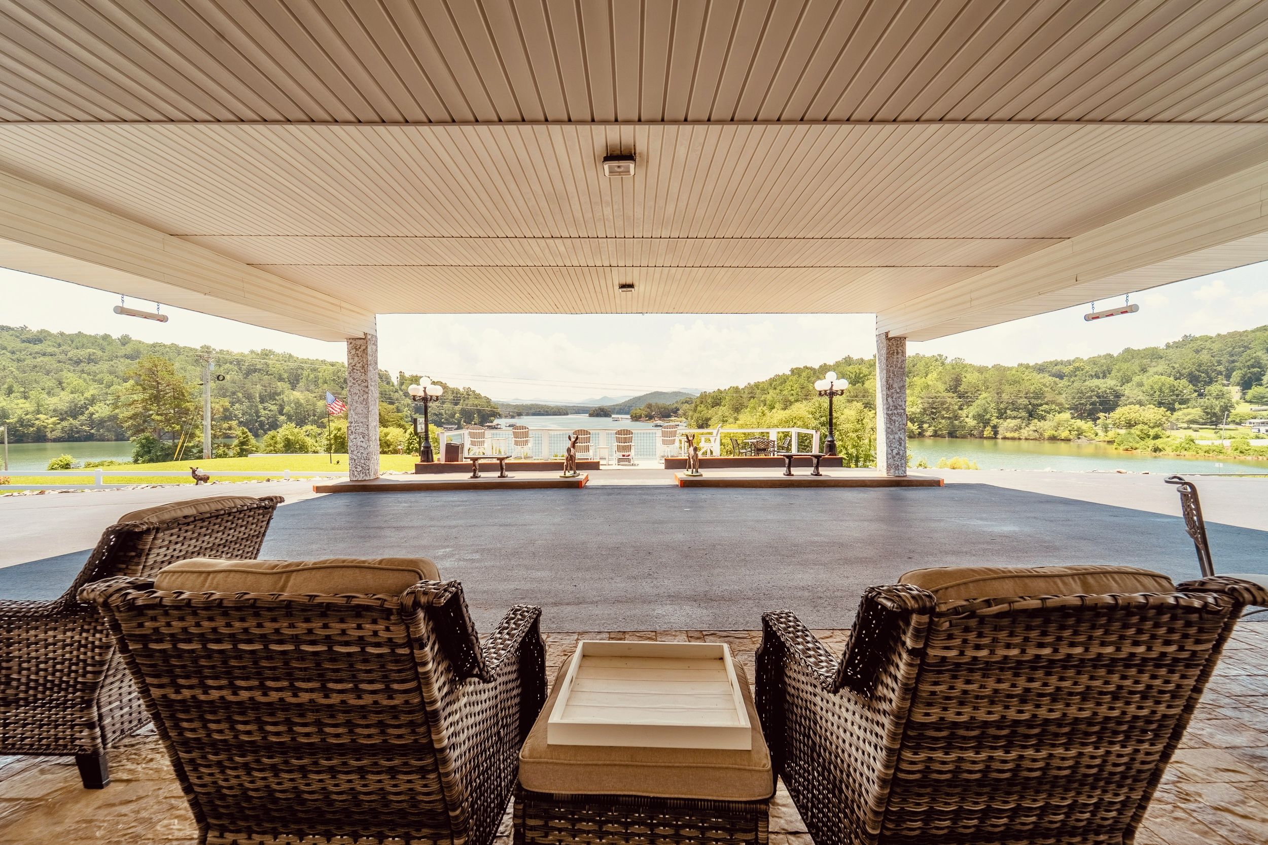 A covered outdoor seating area with wicker furniture and a view of a lake and forest.