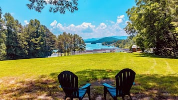 A grassy area with two chairs facing a scenic view of a lake and buildings in the distance.