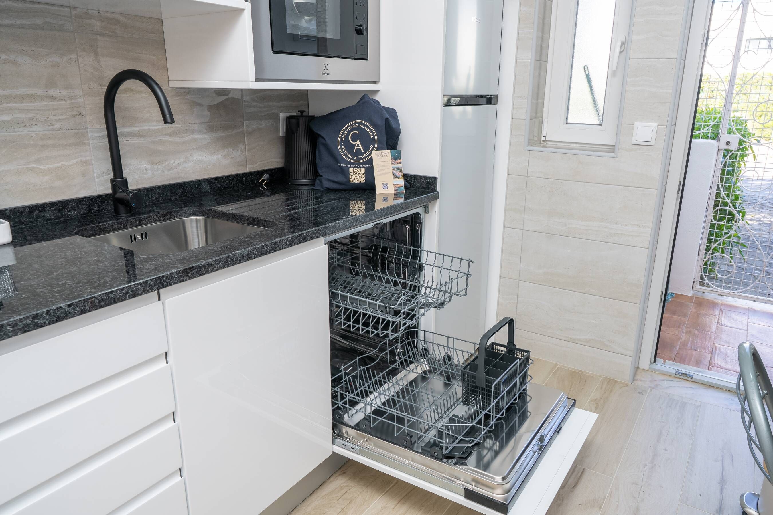A modern kitchen with a black granite countertop, a built-in dishwasher, and a stainless steel sink.