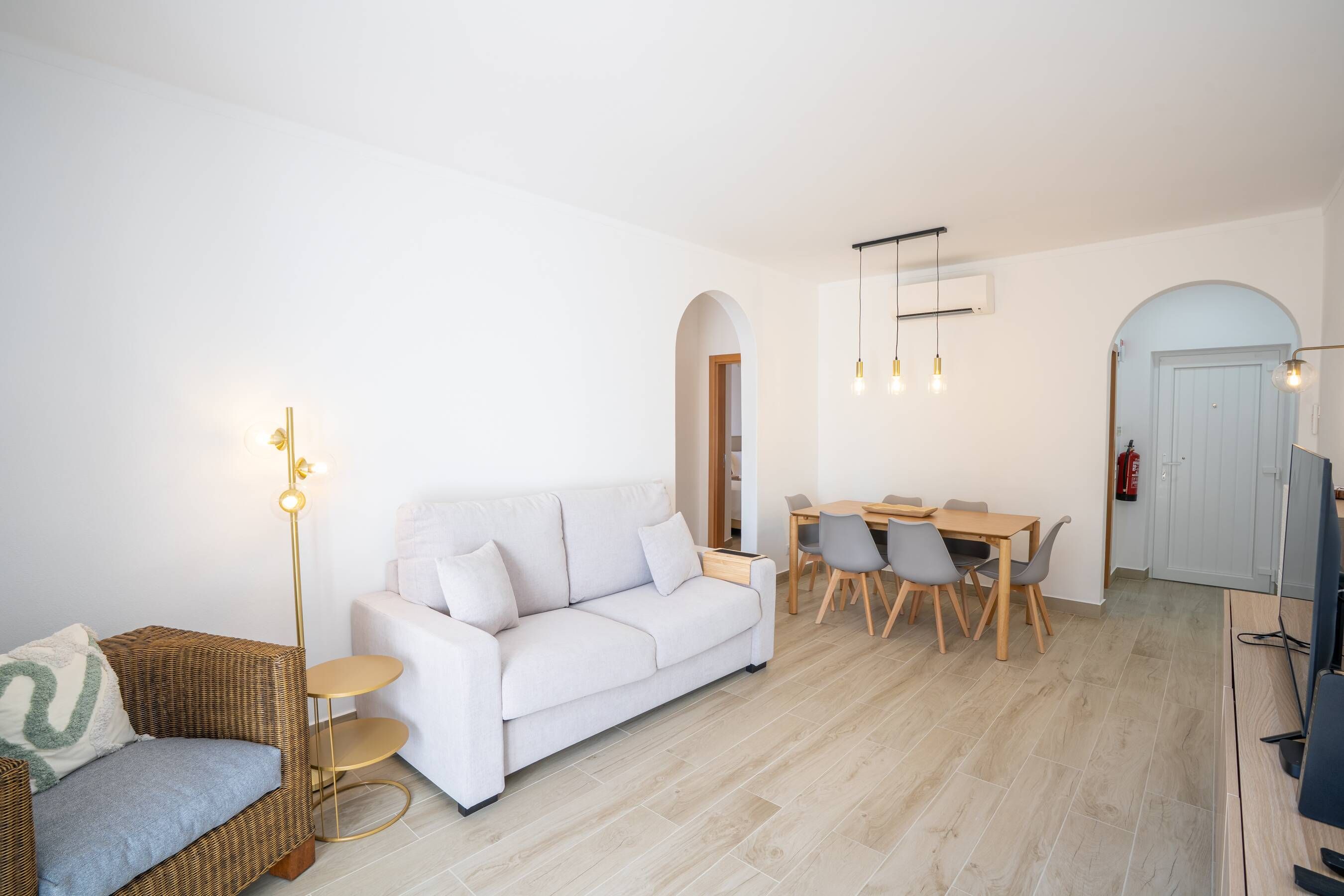 Ein modernes Wohnzimmer mit einem weißen Sofa, einem Esstisch mit Stühlen und einem Korbsessel mit Kissen.