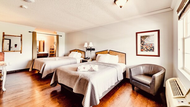A hotel room with two beds, a chair, a desk, a mirror, a picture on the wall, and a window. - Deerfield Inn - Two Queen Beds - Pet Friendly (Hayesville)
