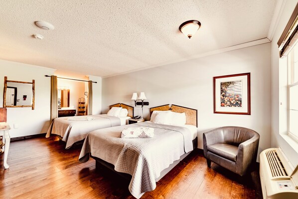 Une chambre d’hôtel avec deux lits, une chaise, un bureau, un miroir, un tableau au mur et une fenêtre.