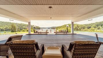 A covered outdoor seating area with wicker furniture and a view of a lake and forest.