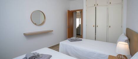 A hotel room with two single beds, a wooden nightstand with a lamp, a mirror on the wall, and a wardrobe with multiple doors.