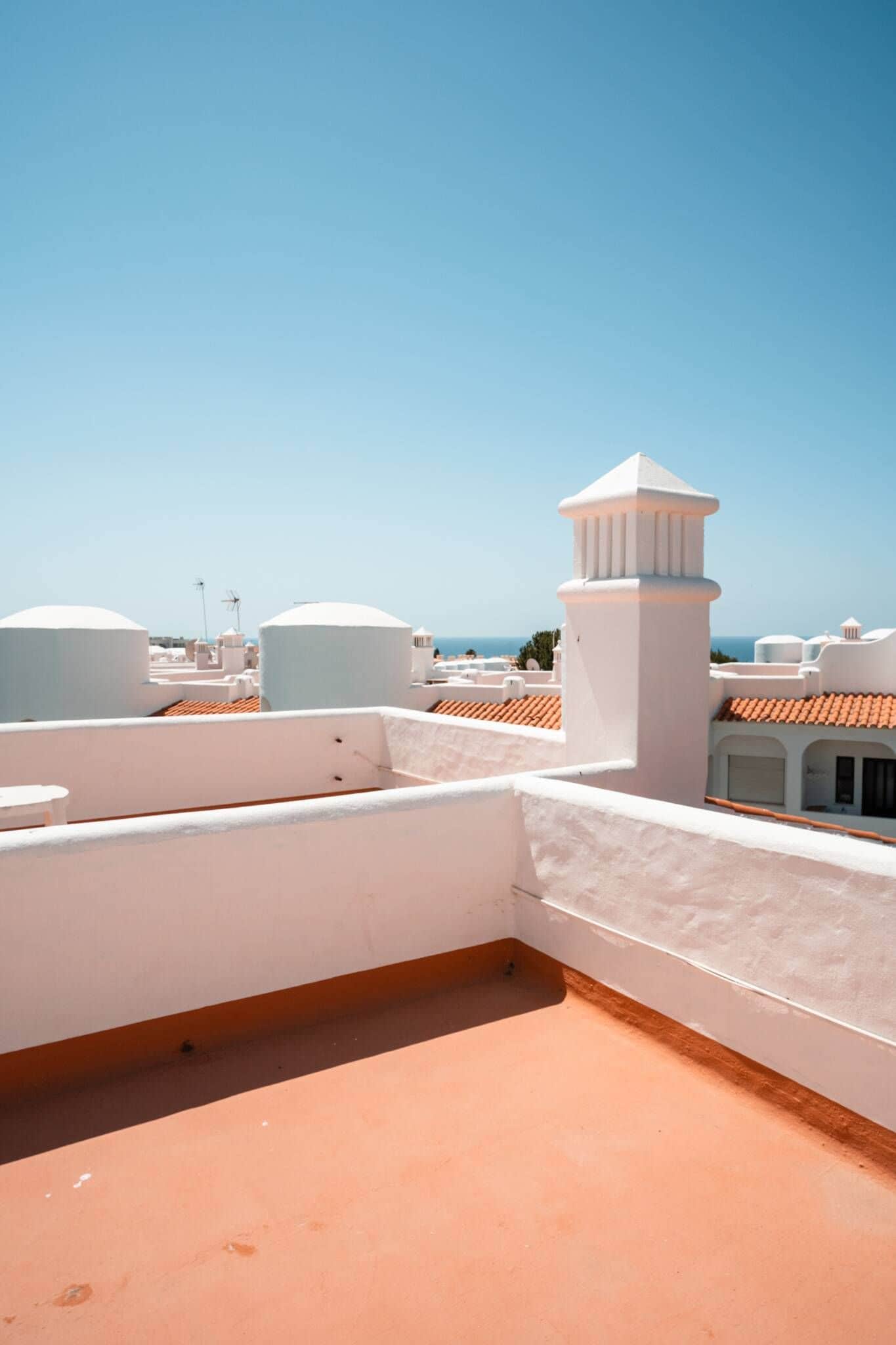 Eine Dachterrasse mit weißer Brüstung, Terrakotta-Dachziegeln und einem strahlend blauen Himmel.