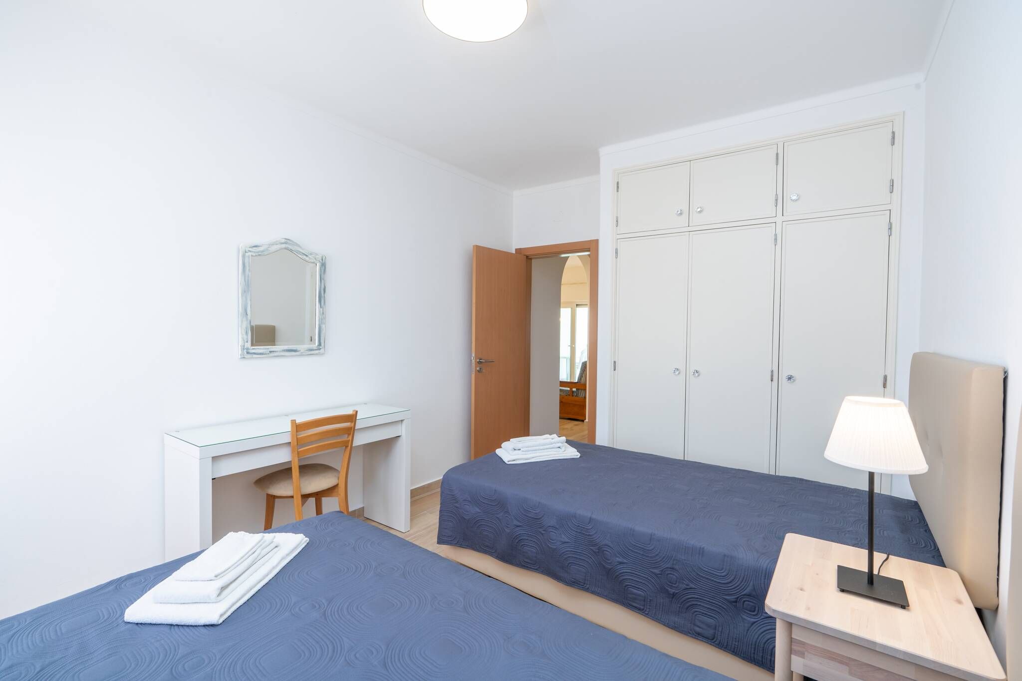 Une chambre avec deux lits, un bureau, une chaise, une armoire et une lampe de chevet.