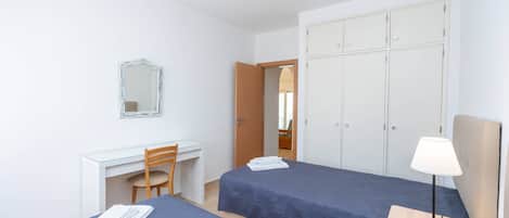 Une chambre avec deux lits, un bureau, une chaise, une armoire et une lampe de chevet.