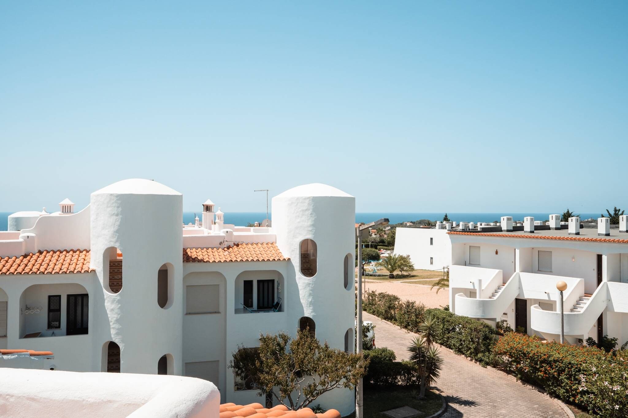 A coastal residential area with white buildings, some with red-tiled roofs, and a clear view of the sea.