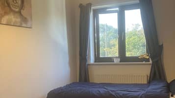 Quarto com duas camas, janela com cortinas, radiador e estátua de Buda na parede.