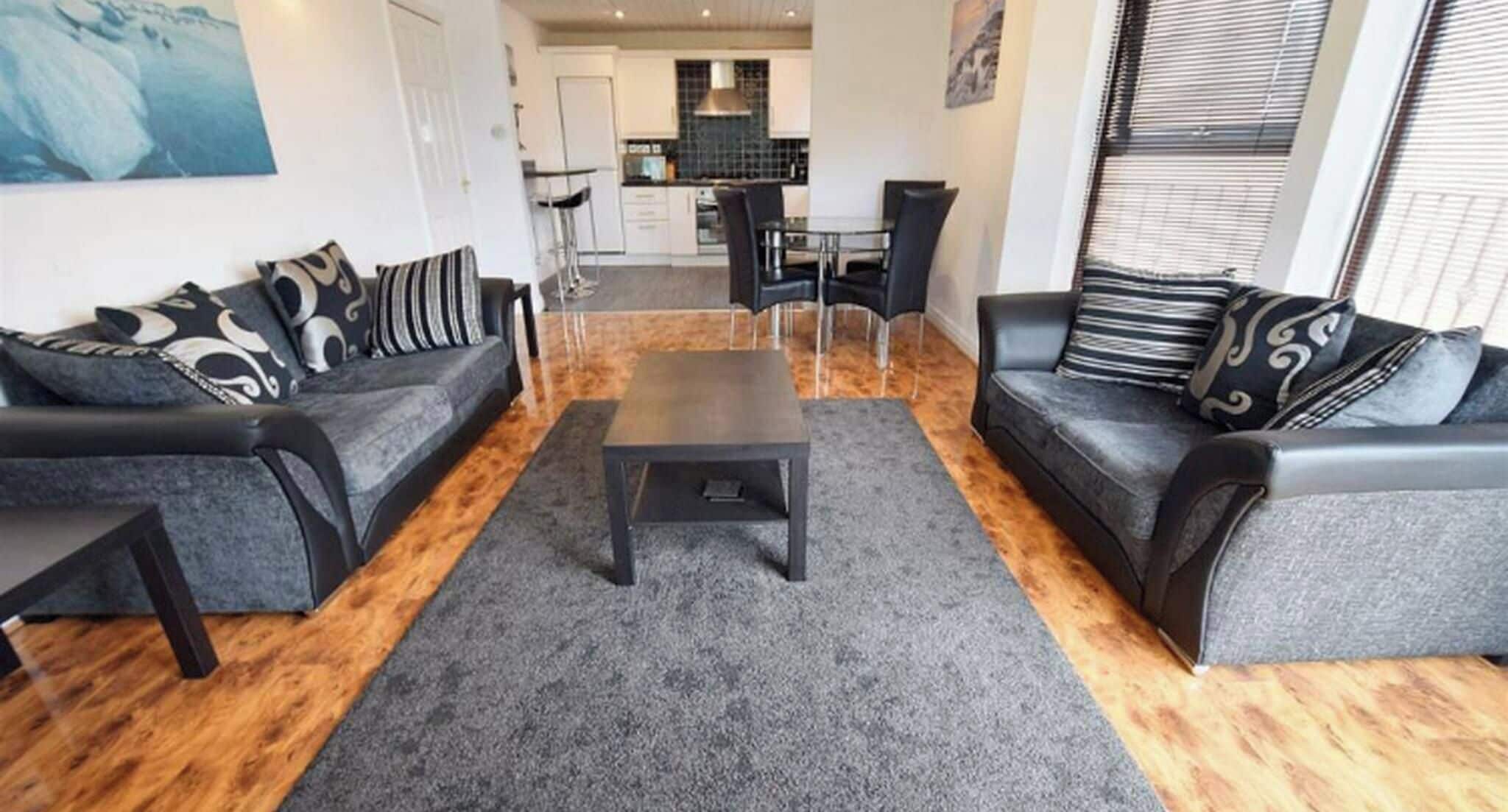 Uma sala de estar moderna com dois sofás, uma mesa de centro e uma área de refeições ao fundo.