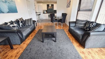 Uma sala de estar moderna com dois sofás, uma mesa de centro e uma área de refeições ao fundo.