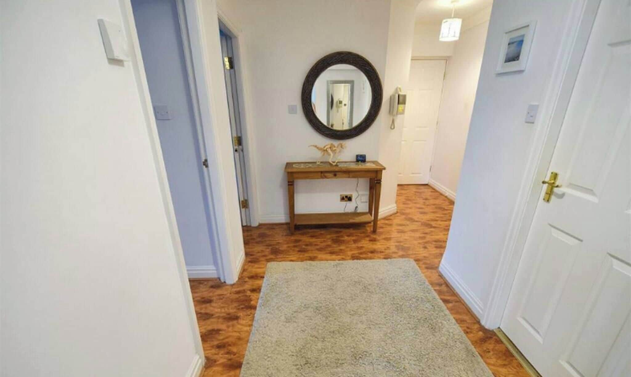 Een gang met een houten console tafel, een spiegel en een vloerkleed.