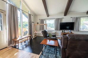 Ein modernes Wohnzimmer mit einer Couch, einem Couchtisch, einer Holzbank, einem Fernseher und einem großen Fenster mit Vorhängen.