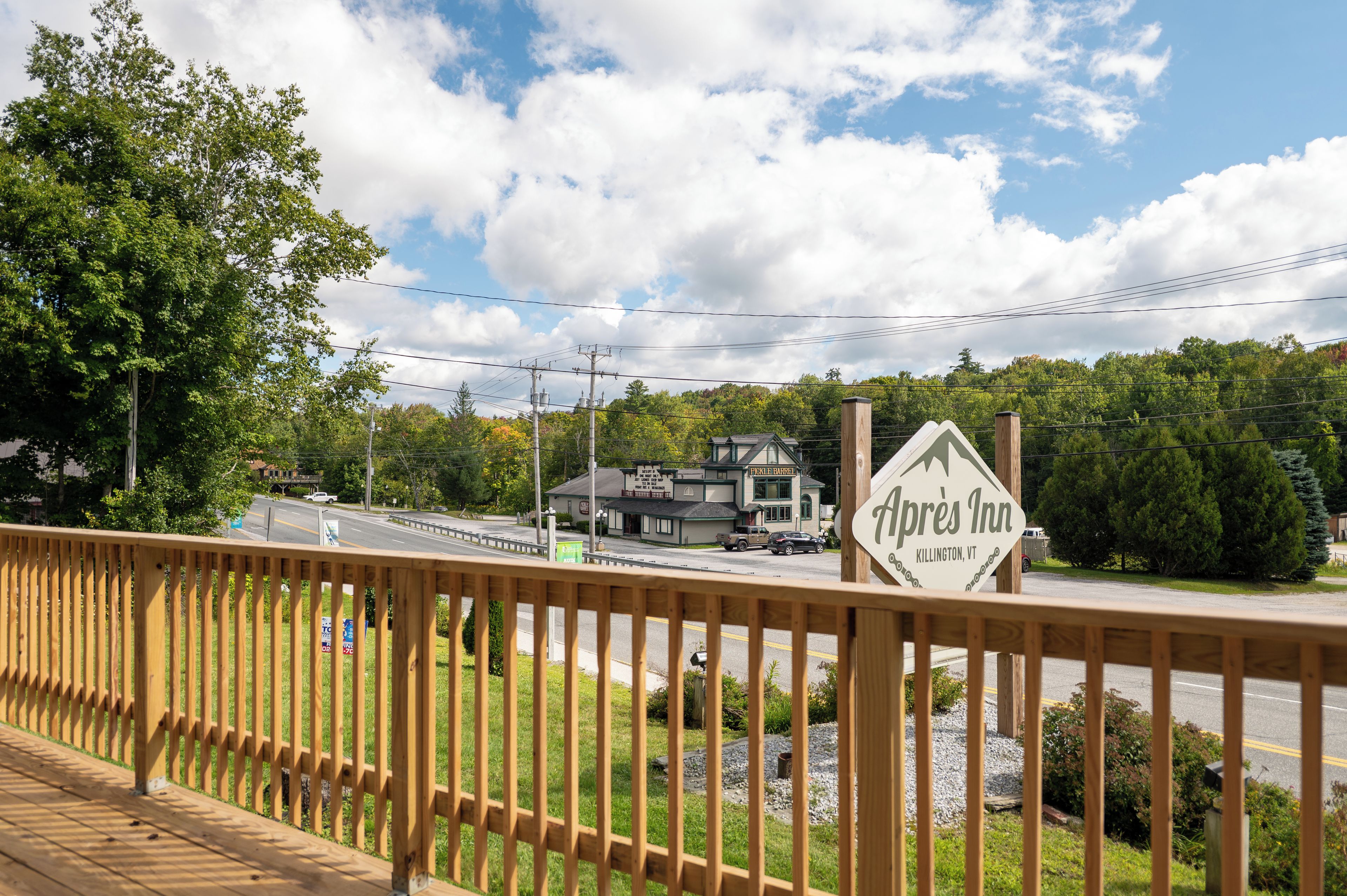 Vista de Apres Inn en Killington, Vermont, con una terraza de madera en primer plano y una carretera con vehículos al fondo.
