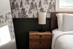 Ein Schlafzimmer mit einem Nachttisch aus Holz, einer weißen Lampe und einem Bett mit weißer Bettwäsche.