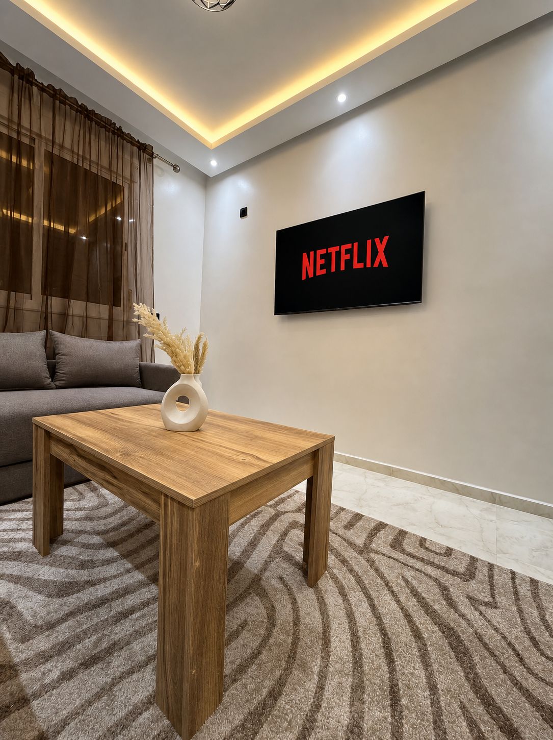 A modern living room with a sofa, a wooden coffee table, and a wall-mounted TV displaying 'NETFLIX'.