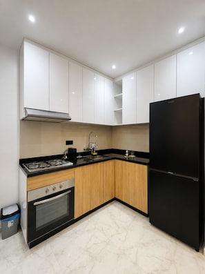 Une cuisine moderne avec des meubles blancs, un réfrigérateur noir, une cuisinière et un four.