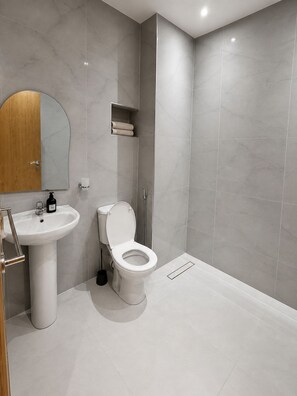 Une salle de bain moderne avec un lavabo, des toilettes et une zone de douche, le tout de couleur blanche.
