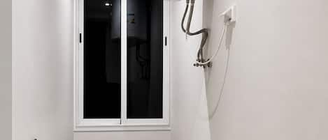 A compact laundry room with a front-loading washing machine, a window, and a wall-mounted water heater.
