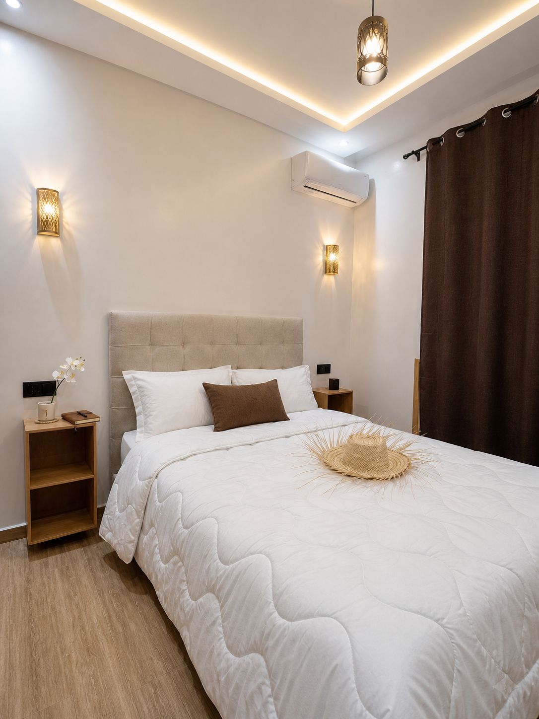A bedroom with a large bed, bedside tables, wall-mounted lights, an air conditioning unit, and a window with curtains.