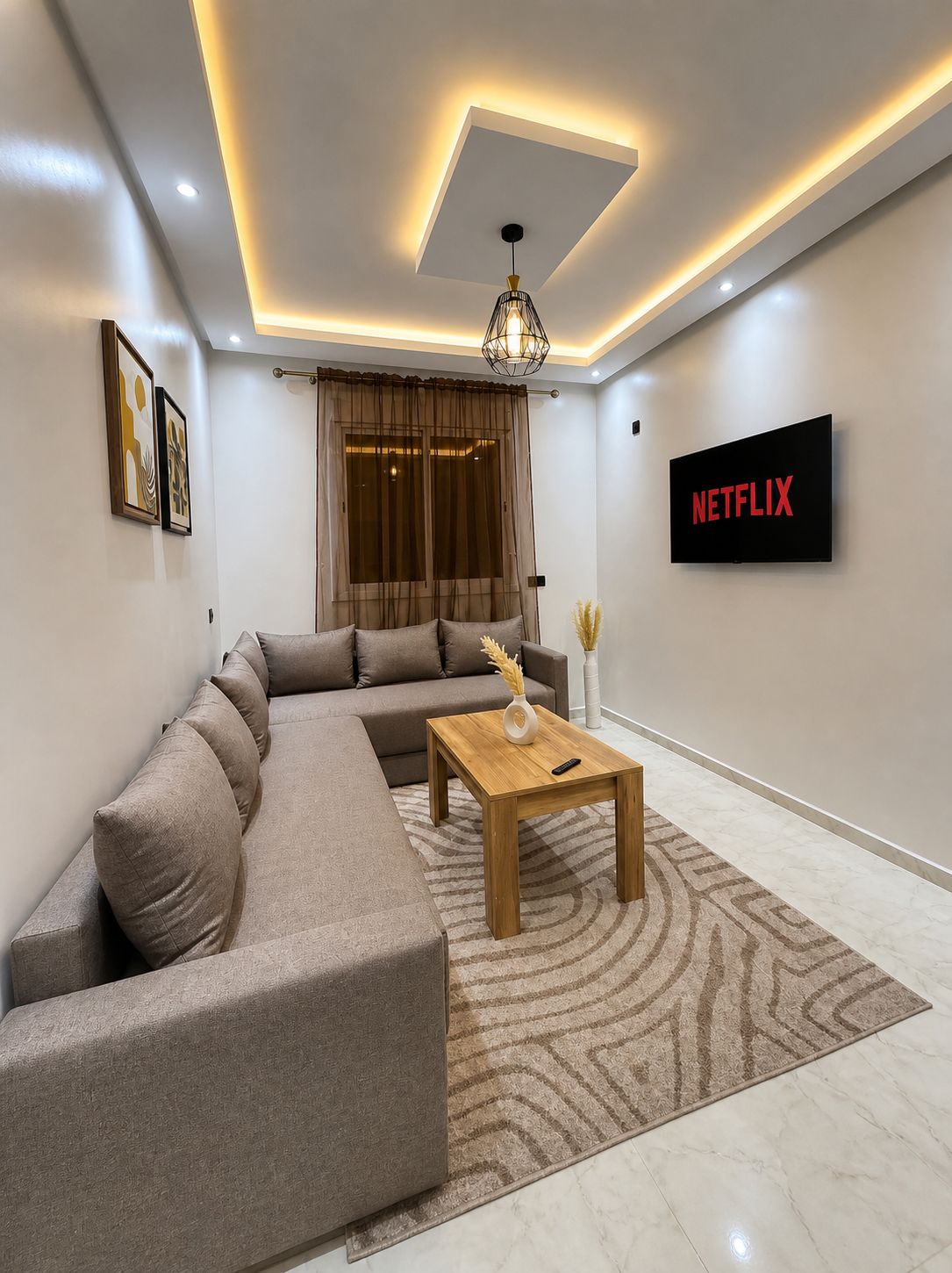 A modern living room with a sectional sofa, a wooden coffee table, a TV mounted on the wall, and a ceiling light fixture.