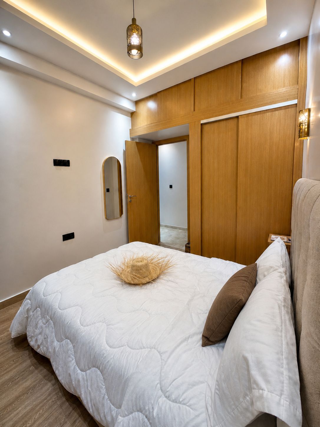 Ein modernes Schlafzimmer mit einem großen Bett, Holzpaneelen, einer Deckenleuchte und einem Spiegel an der Wand.