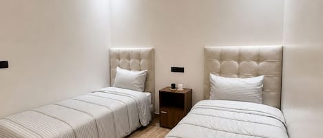 A bedroom with two beds, a nightstand, and a hanging light fixture.