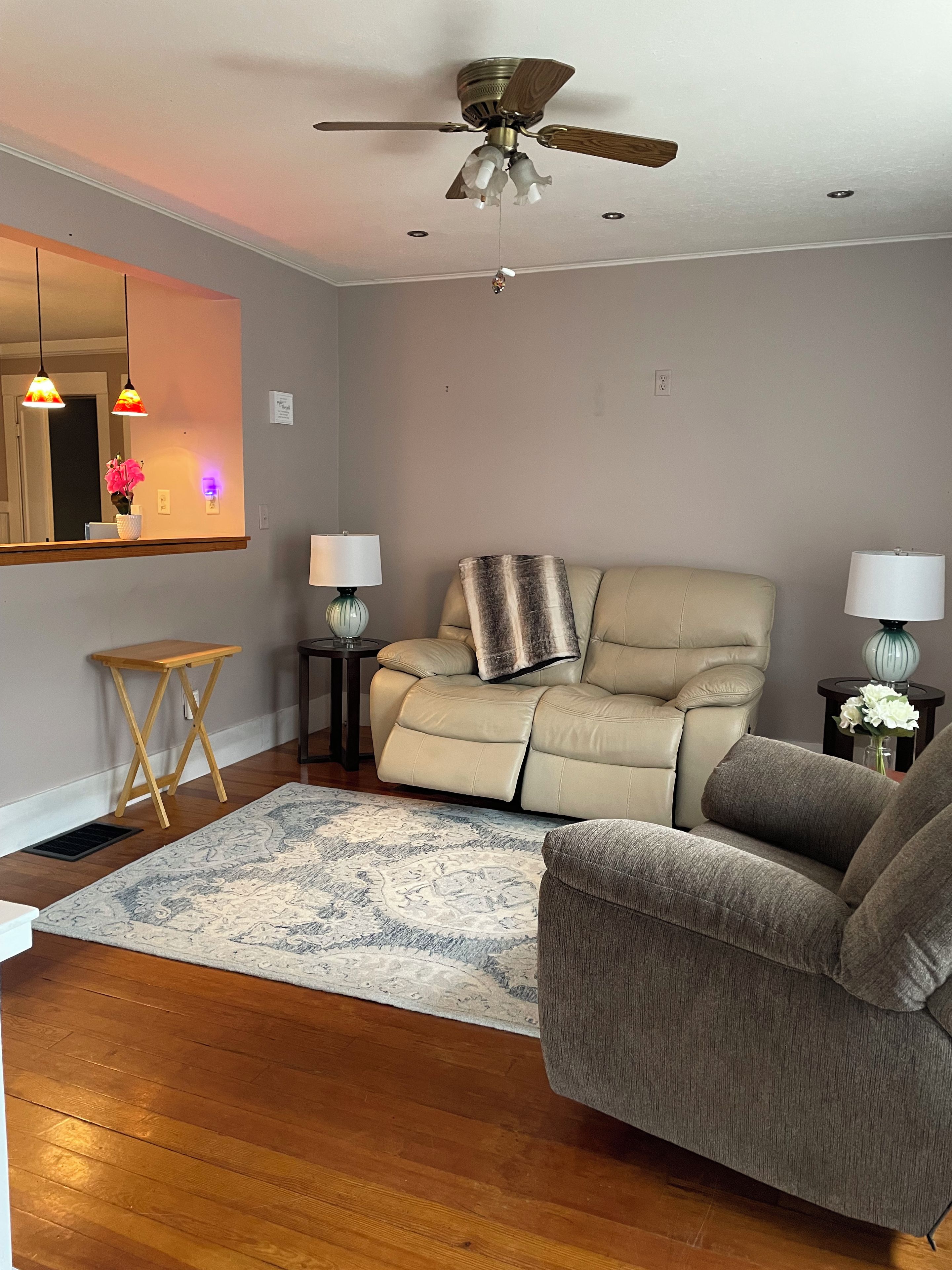 A living room with a beige sofa, two side tables with lamps, a wooden coffee table, a patterned rug, and a ceiling fan.