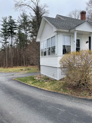 A small, single-story house with a sloped roof, a front porch, and a chimney. - Cozy 1-bedroom house on a quiet property near shopping with off street parking (Bedford)
