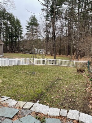 A residential yard with a white picket fence, a stone border, and a grassy area with trees in the background. - Cozy 1-bedroom house on a quiet property near shopping with off street parking (Bedford)