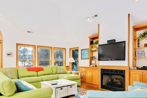 Een woonkamer met een groene bank, een flatscreen televisie, houten planken en een open haard.