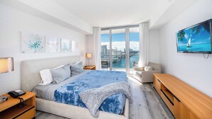 Ein modernes Hotelzimmer mit einem großen Bett, einem Fernseher, einem Schreibtisch und Blick auf die Stadt.