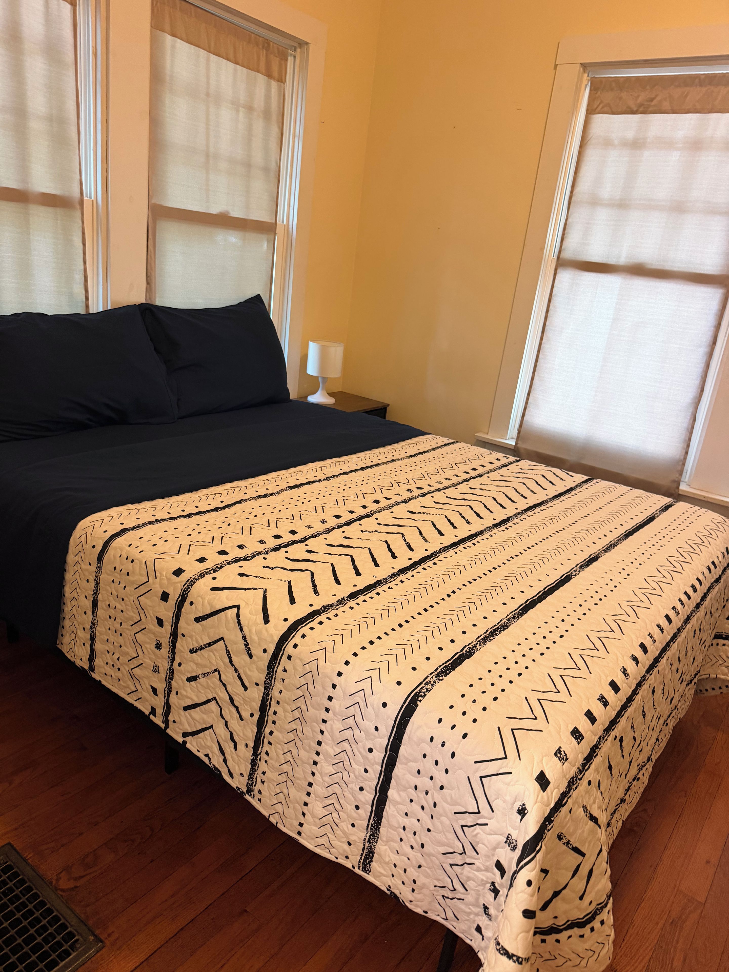 Un dormitorio con cama, mesita de noche y ventana con cortinas.