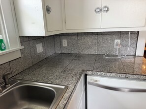 Eine Küche mit Granit Arbeitsplatten, einer Edelstahl-Spüle, weißen Schränken und einem eingebauten Geschirrspüler.