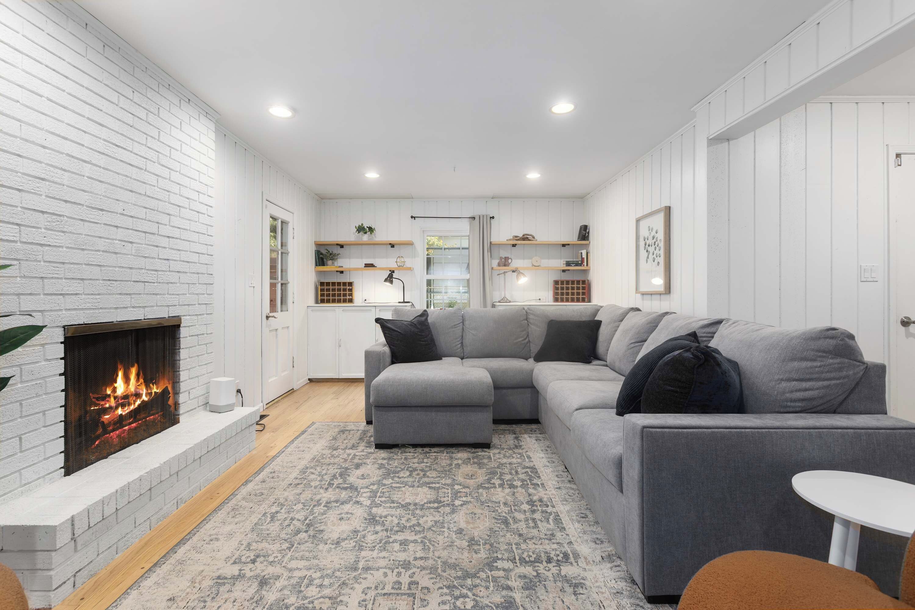 Una sala moderna con chimenea, sofá gris y paredes blancas.