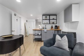 Ein modernes Wohnzimmer mit einem grauen Sofa, einem schwarzen runden Tisch und einer Küchenzeile mit einer Holzausstattung und grauen Schränken.
