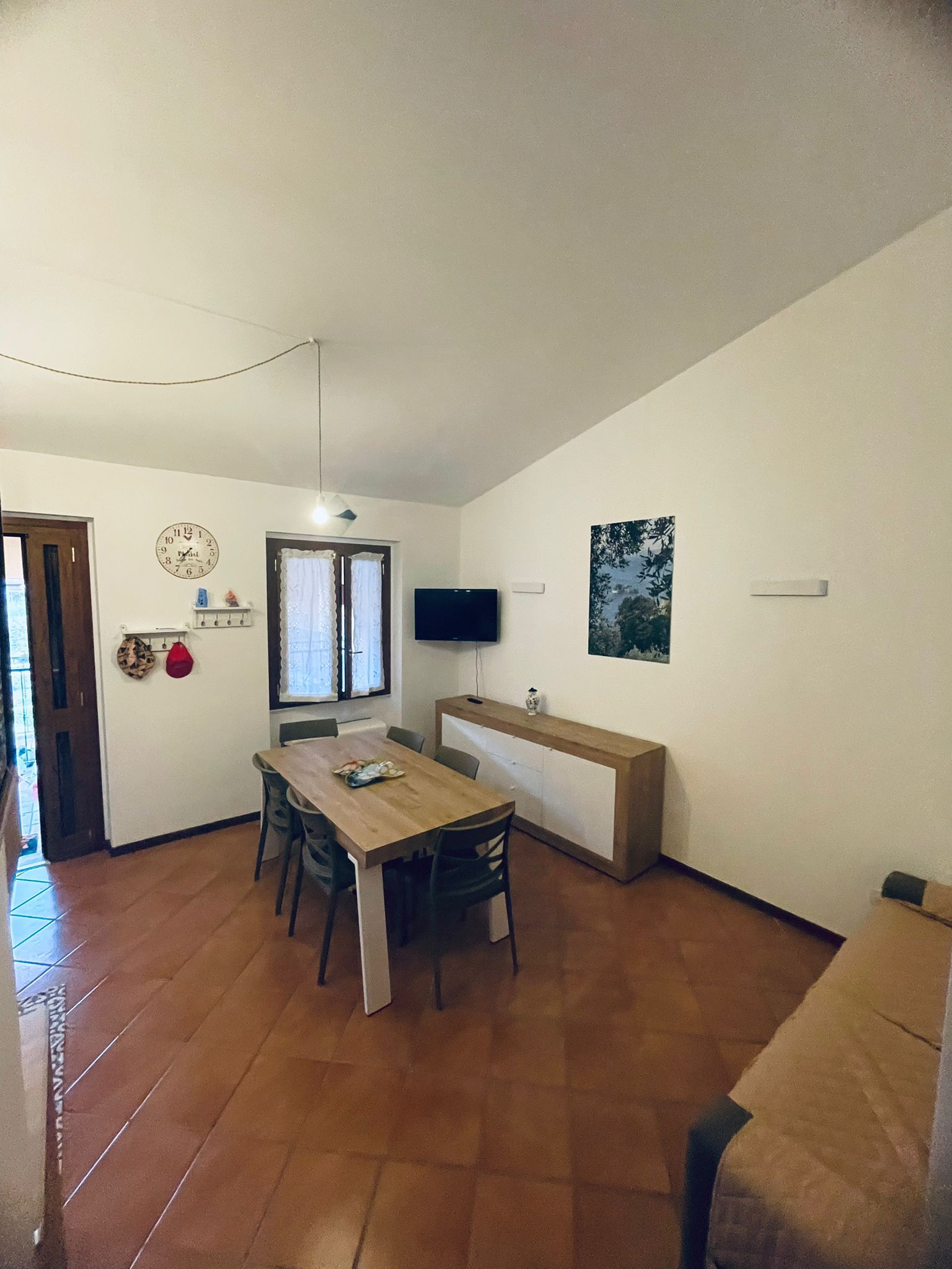 Un coin repas avec une table et des chaises en bois, un téléviseur fixé au mur et une fenêtre avec des rideaux.