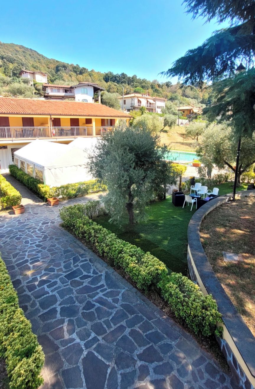 Un sentiero in pietra conduce a una zona piscina con una tenda bianca, immersa nel verde e con edifici residenziali sullo sfondo.