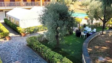 Un sentiero in pietra conduce a una zona piscina con una tenda bianca, immersa nel verde e con edifici residenziali sullo sfondo.