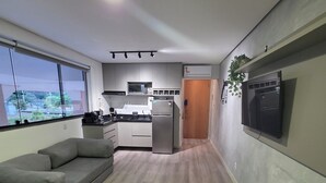 Cocina moderna con refrigerador, microondas y lavamanos. Hay un sofá gris y una mesita con un control remoto.
